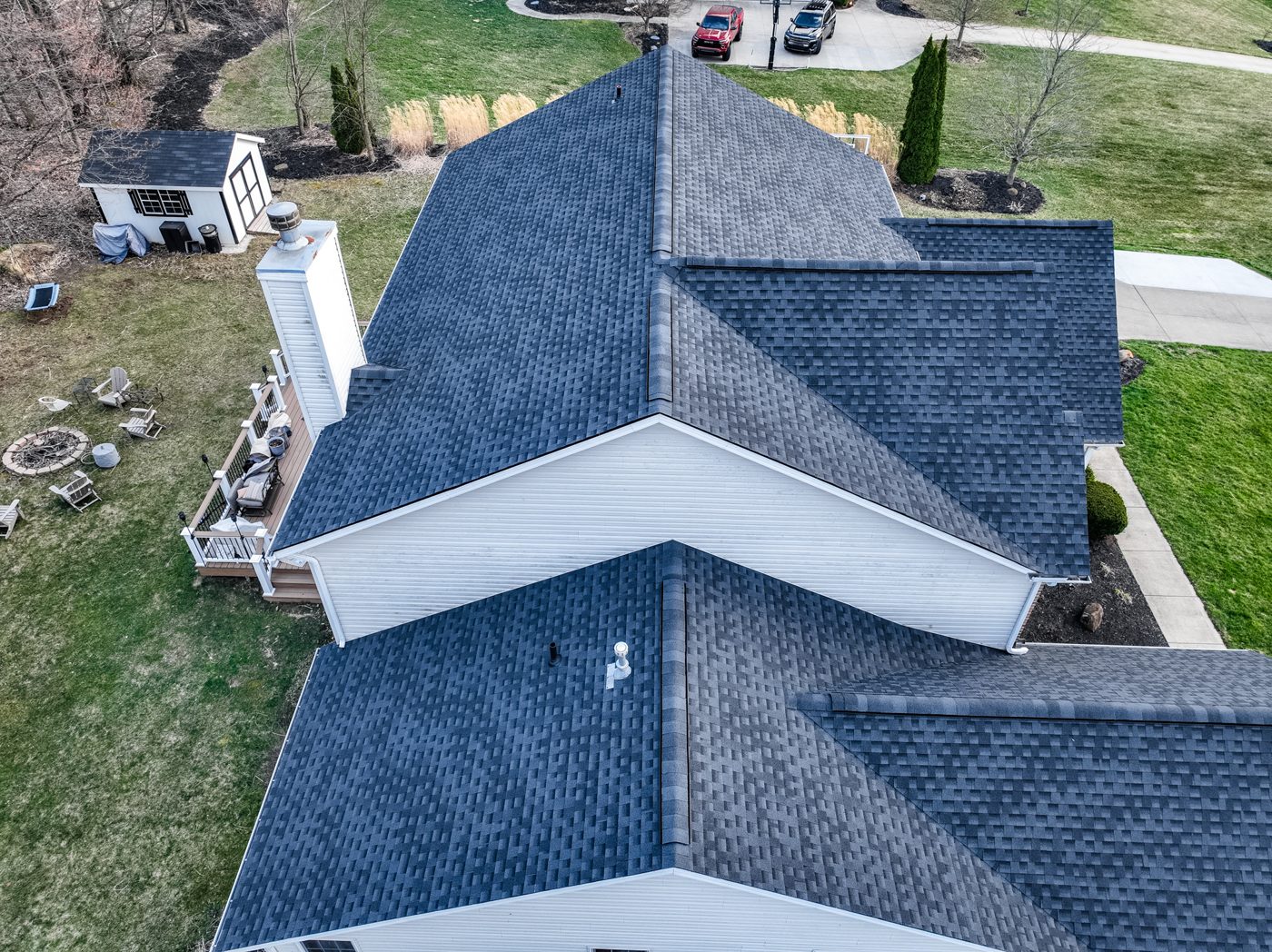 Close aerial drone photo of a completed shingle roof meeting white siding gables and a brick chimney